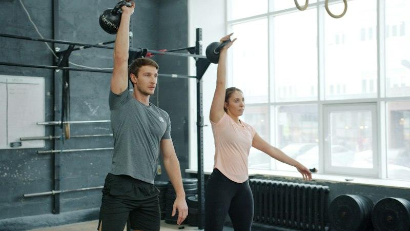 Dues persones aixecant kettlebells per sobre del cap